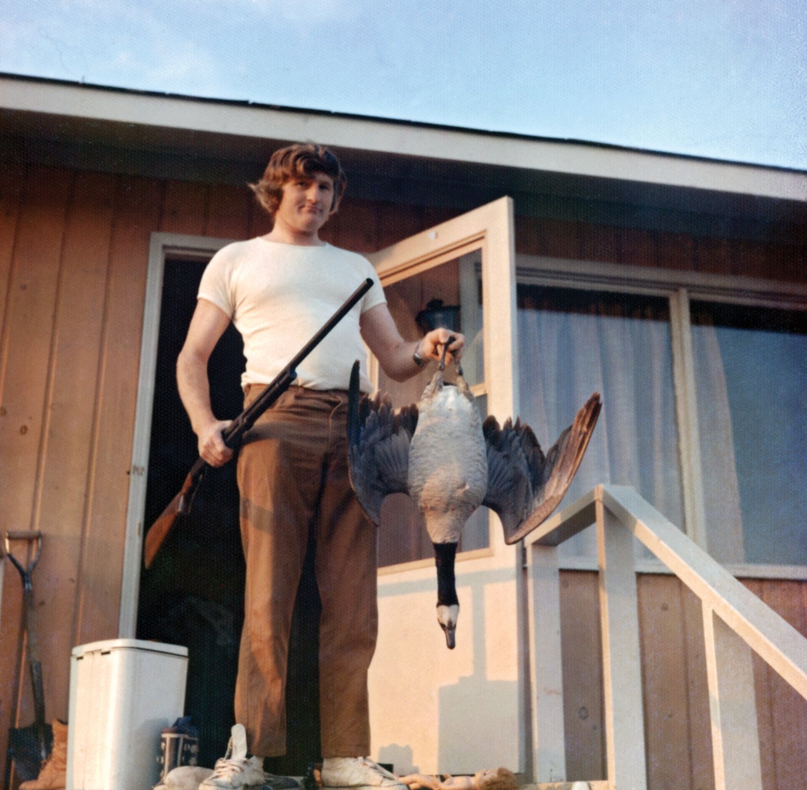 Patrick Mulrooney with gun and goose on porch of teacherage after having shot dinner, Ogoki, 1975. Photo by Mary Mulrooney.
